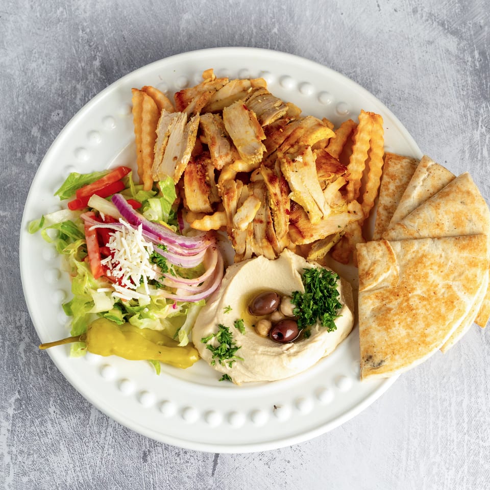 Chicken shawarma plate with fries, hummus, pita bread, salad, and a pepper on a white plate.