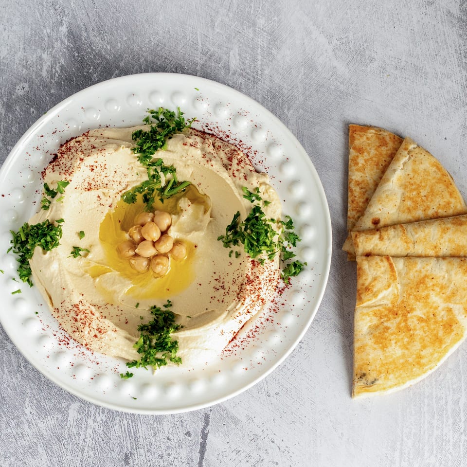 Creamy hummus with chickpeas, olive oil, parsley, and paprika, served with pita bread.