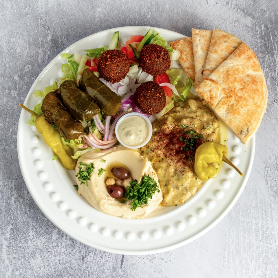 A white plate with falafel, stuffed grape leaves, hummus, baba ghanoush, salad, and pita bread.