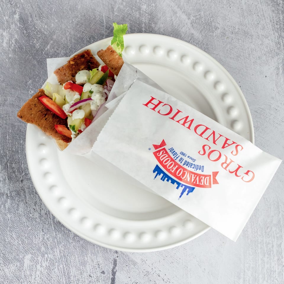 Devanco Foods Gyros Sandwich, filled with meat, lettuce, tomatoes, onions, and tzatziki sauce, on a white plate.