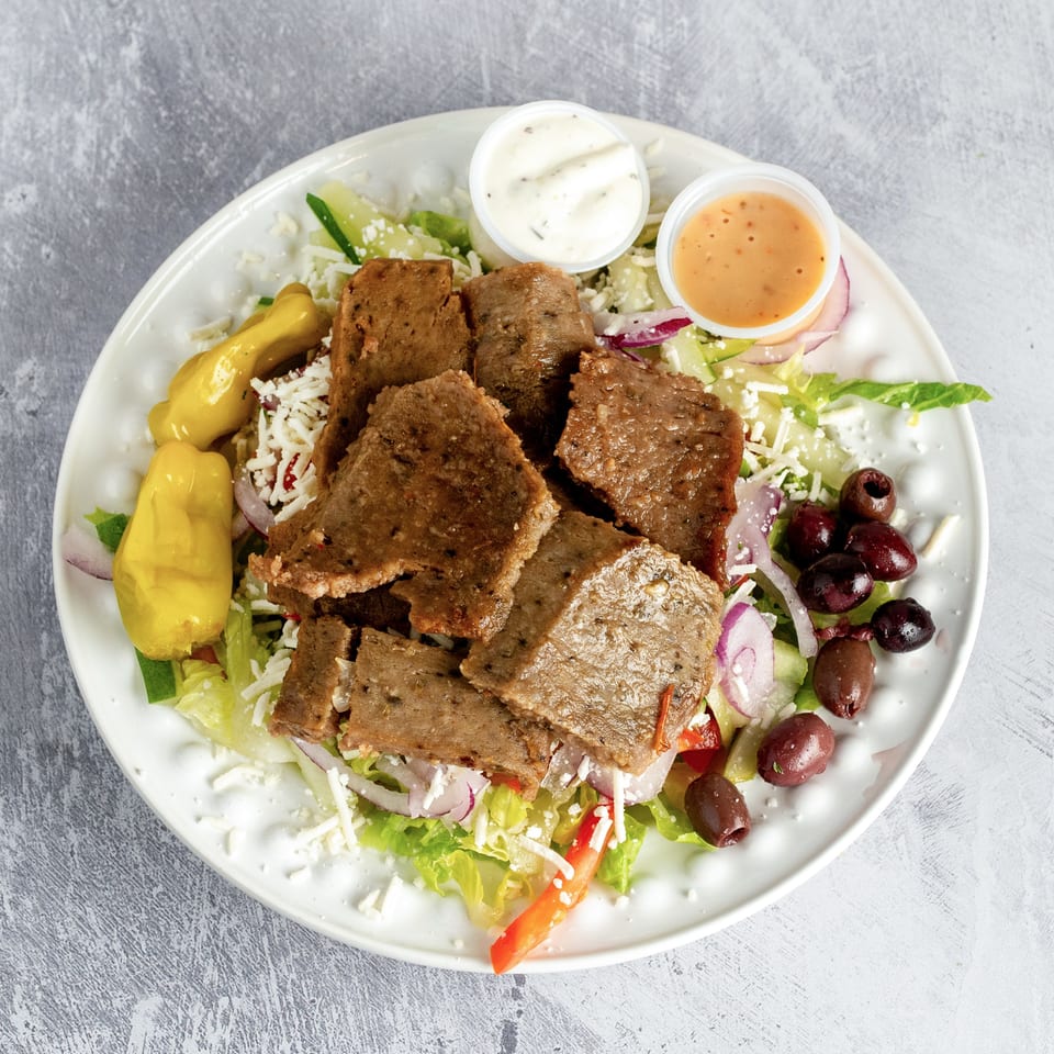 Gyro meat salad with lettuce, onions, peppers, olives, feta cheese, and two dressings.