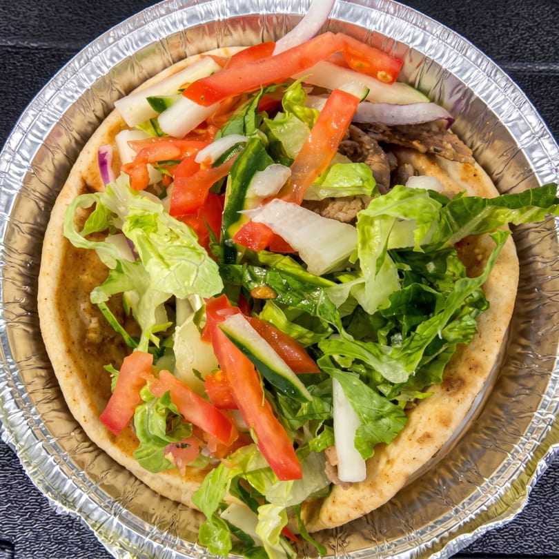 Gyro in a foil container, filled with meat, lettuce, tomatoes, and onions.