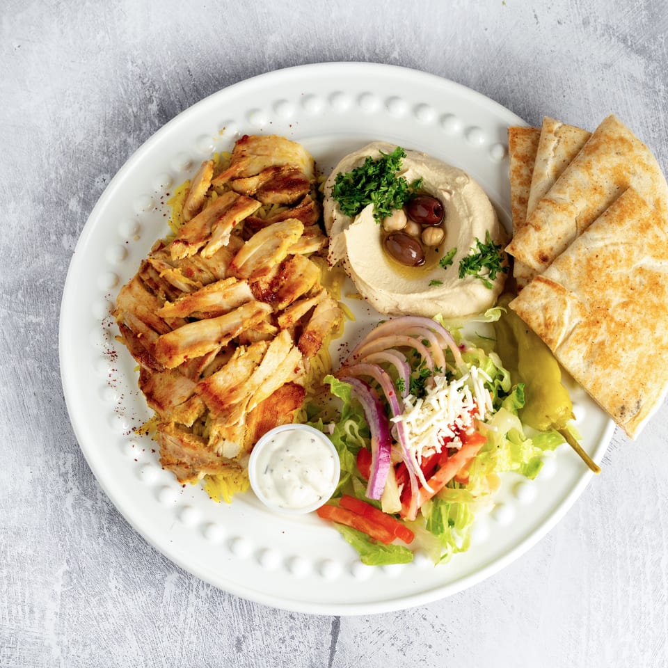 Chicken shawarma plate with hummus, pita bread, salad, and a side of sauce.
